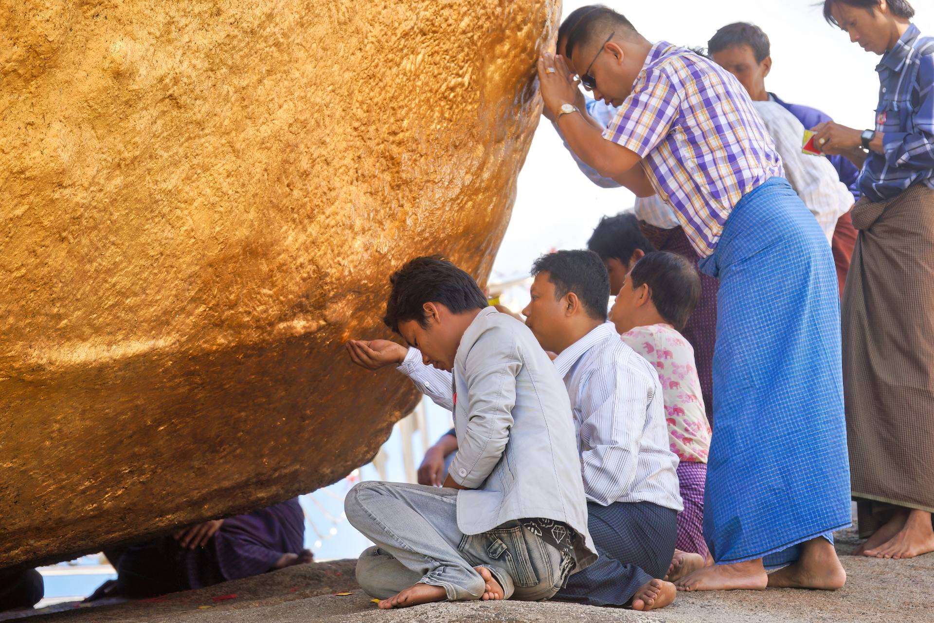 Männer im Gebet am Goldenen Felsen. Als Opfergabe bringen sie hauchdünne Goldfolie am Felsen an.
